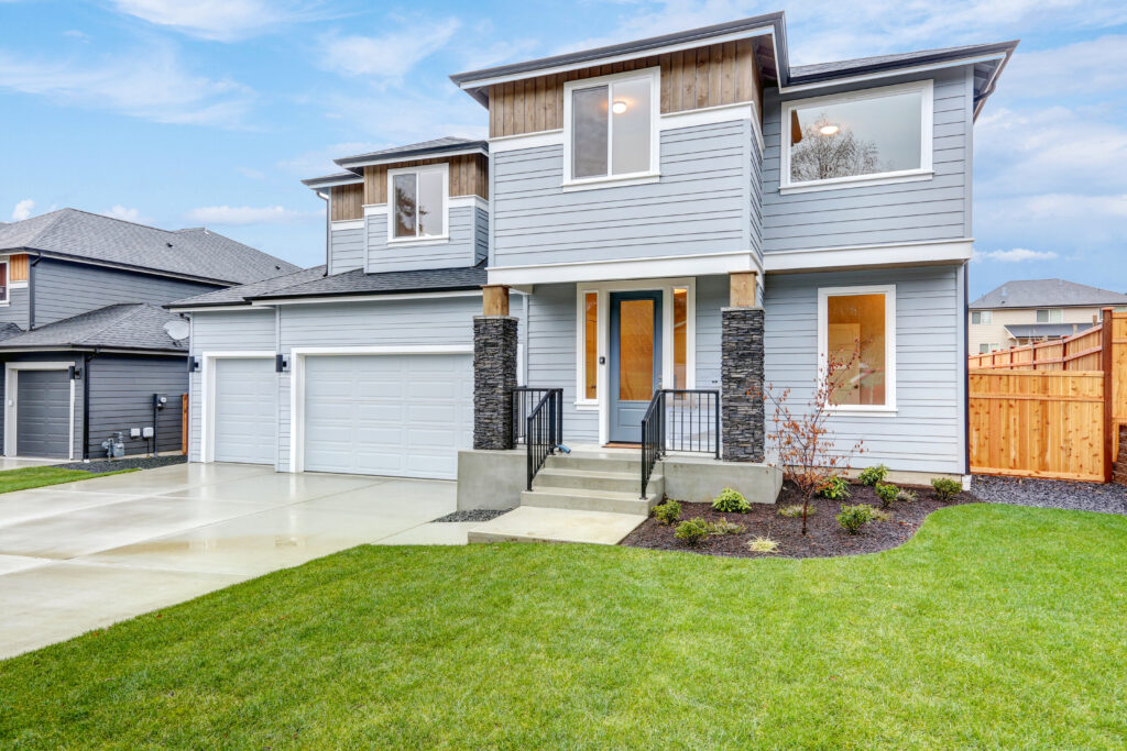 Modern two-story house with gray siding, large windows, and a three-car garage. The green lawn and clean driveway enhance its inviting look.